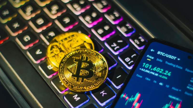 Close-up of gold Bitcoin coins on a backlit keyboard with trading app on smartphone., tags: digital traditional - pexel