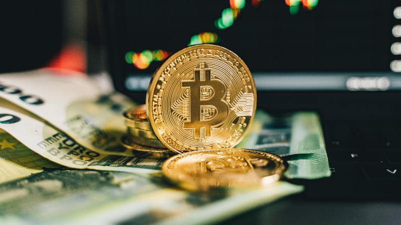 Close-up of Bitcoin and Euro notes on laptop keyboard with market chart in background., tags: ai tokens - pexel