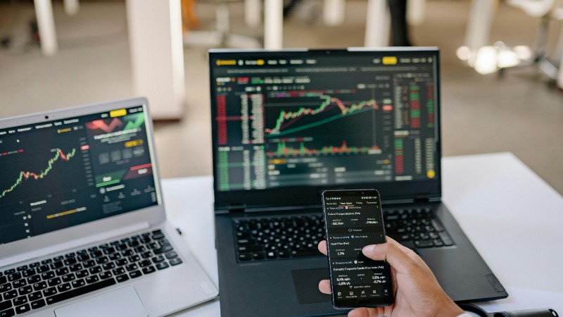 A professional tracks stock market trends using two laptops and a smartphone, showcasing digital finance tools., tags: economic growth persistent - pexel