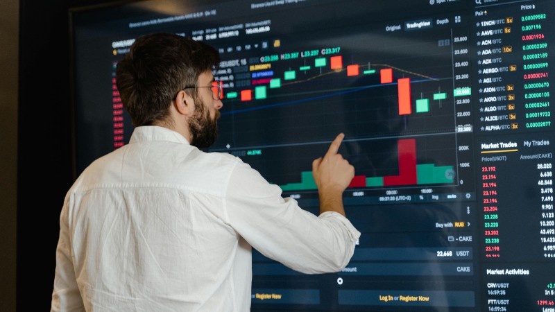 A man analyzes cryptocurrency graphs on a touchscreen monitor in a modern office setting., tags: navigating market trends investment - pexel