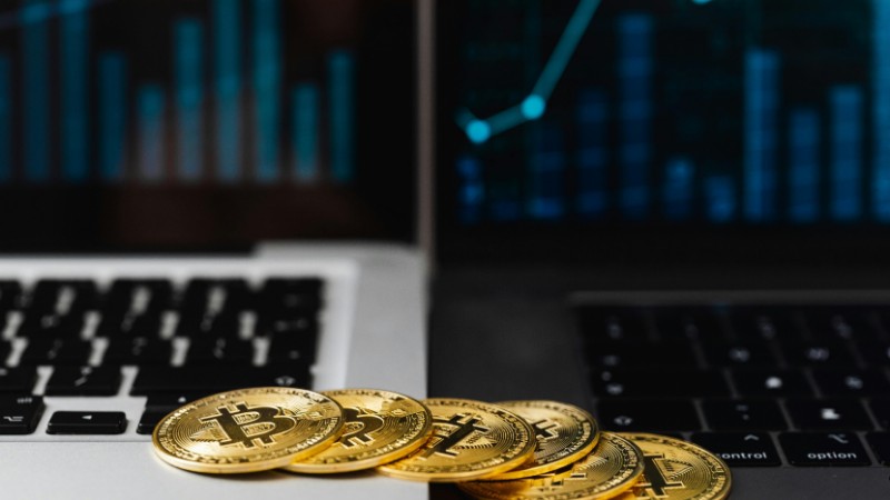 Gold bitcoins placed on laptop keyboards with digital financial graphs in the background., tags: retail - pexel