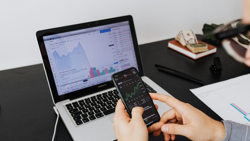 Person analyzing stock market data on a laptop and smartphone indoors., tags: insights - pexel