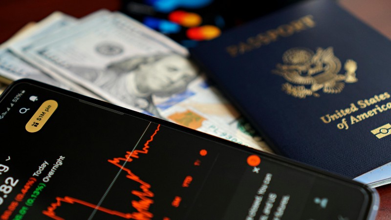 Close-up of smartphone with stock chart, cash, and US passport, symbolizing travel and finance., tags: u.s. economy - pexel