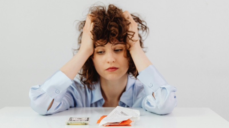 Woman in blue sleeves appears stressed while looking at receipts and money, symbolizing financial stress., tags: slower capital flows persistent - pexel
