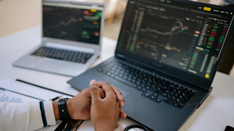 Man seated at a desk using laptops to monitor stock market trends and investments., tags: fintech - pexel