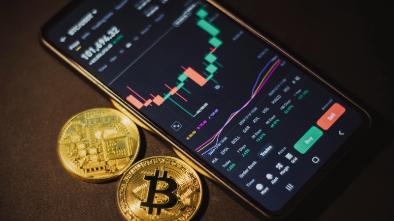 Smartphone displaying trading app with Bitcoin coins on a dark surface., tags: crypto uk regulation - pexel