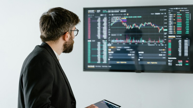Man observing stock market data on a screen and holding a tablet, representing financial analysis and trading., tags: long-term - pexel