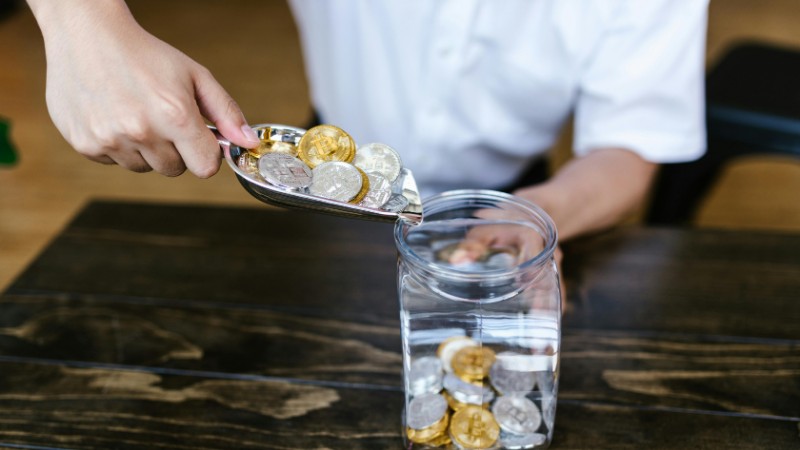 Hand placing gold and silver coins into a glass jar on a wooden table indoors., tags: texas banks tokenized deposits - pexel